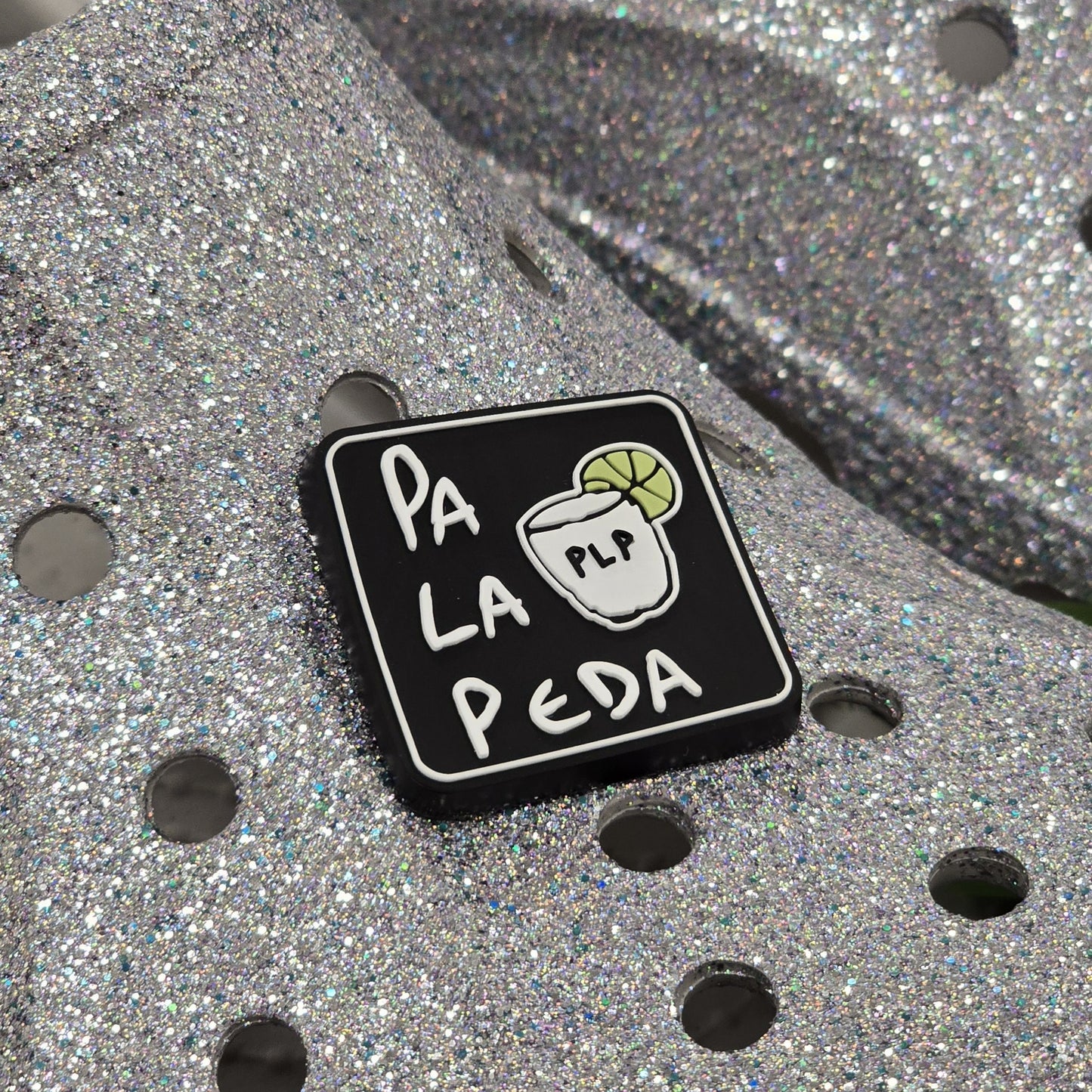 Black square pin with 'Pa La Peda' text and a logo on a metallic surface