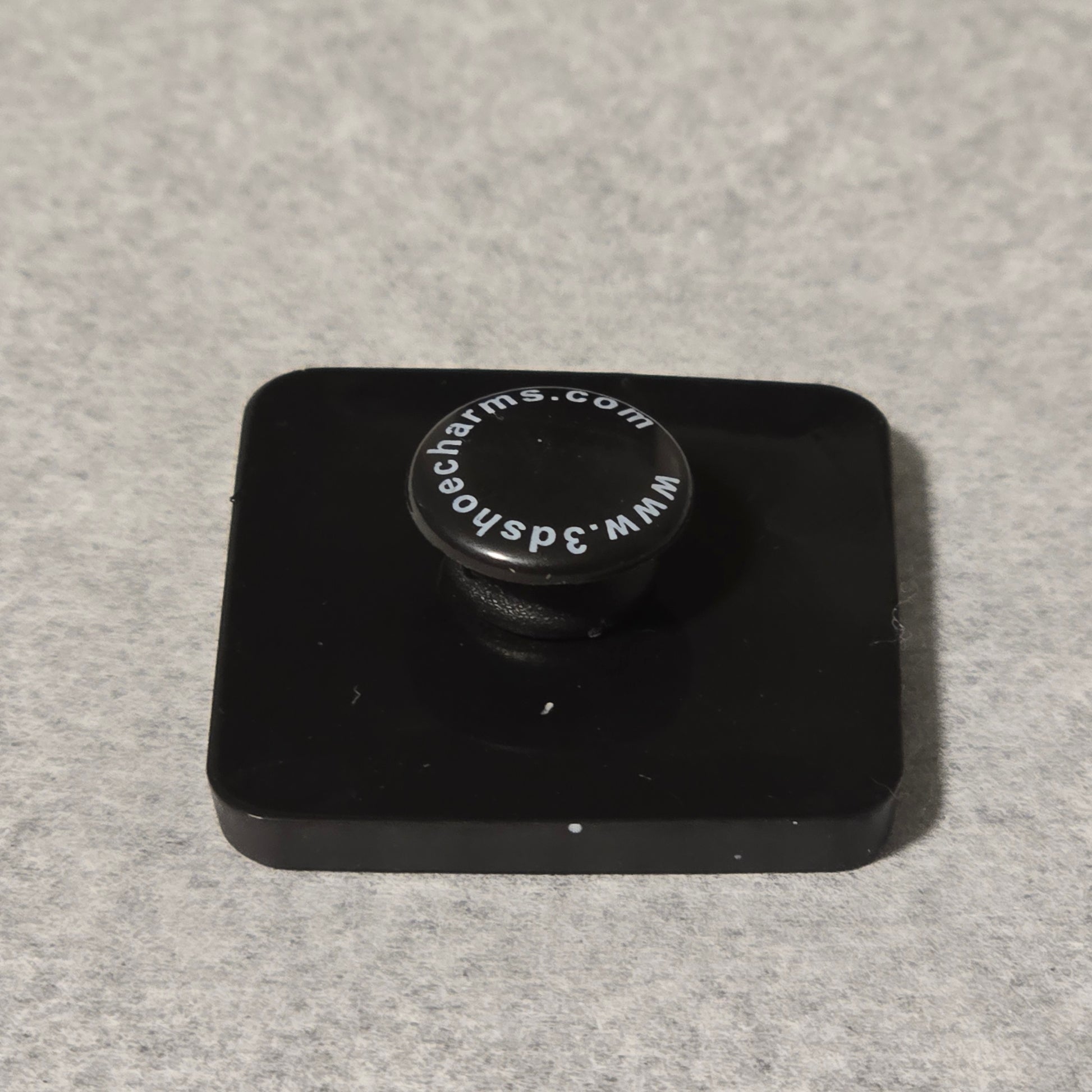 Black square object with a circular component on a gray background