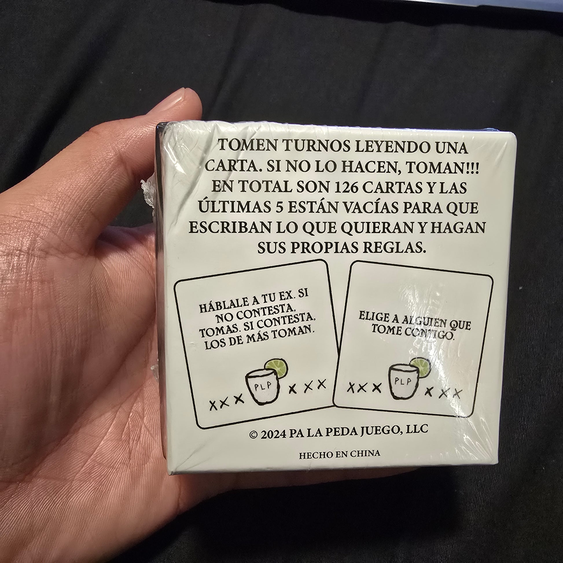 Hand holding a wrapped card game box with text and graphics on a dark background