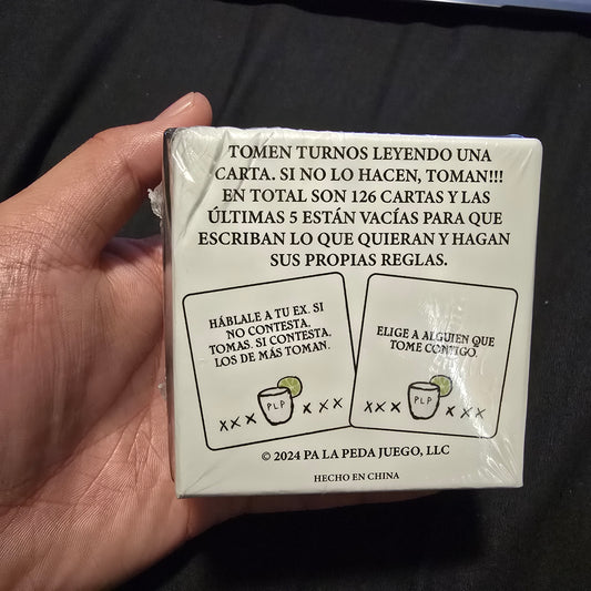 Hand holding a wrapped card game box with text and graphics on a dark background