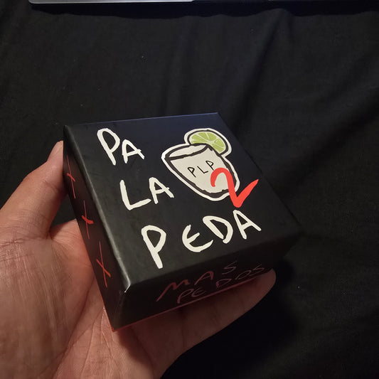 Hand holding a small black box with white text and graphics on a dark background