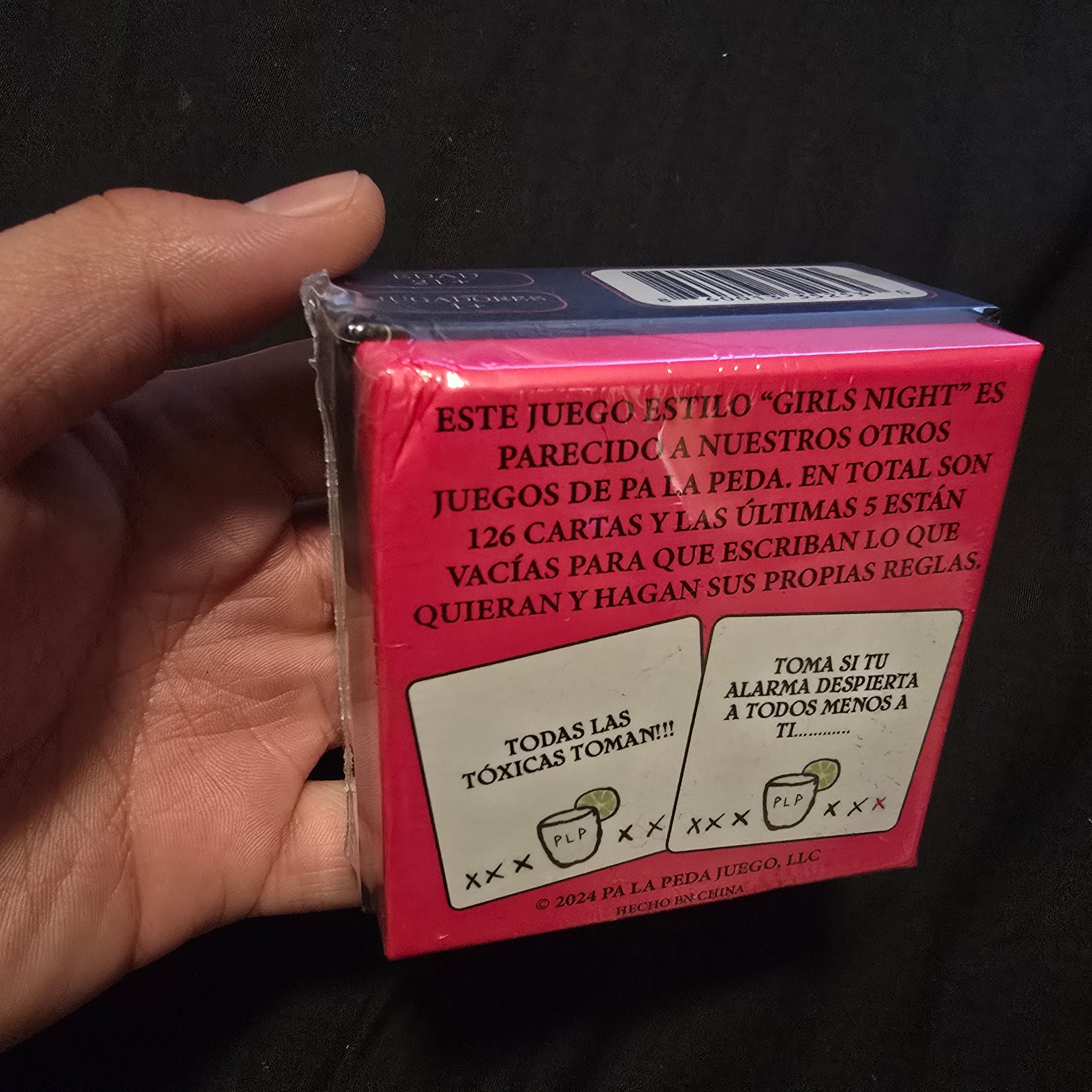 Hand holding a pink card game box with text on a dark background
