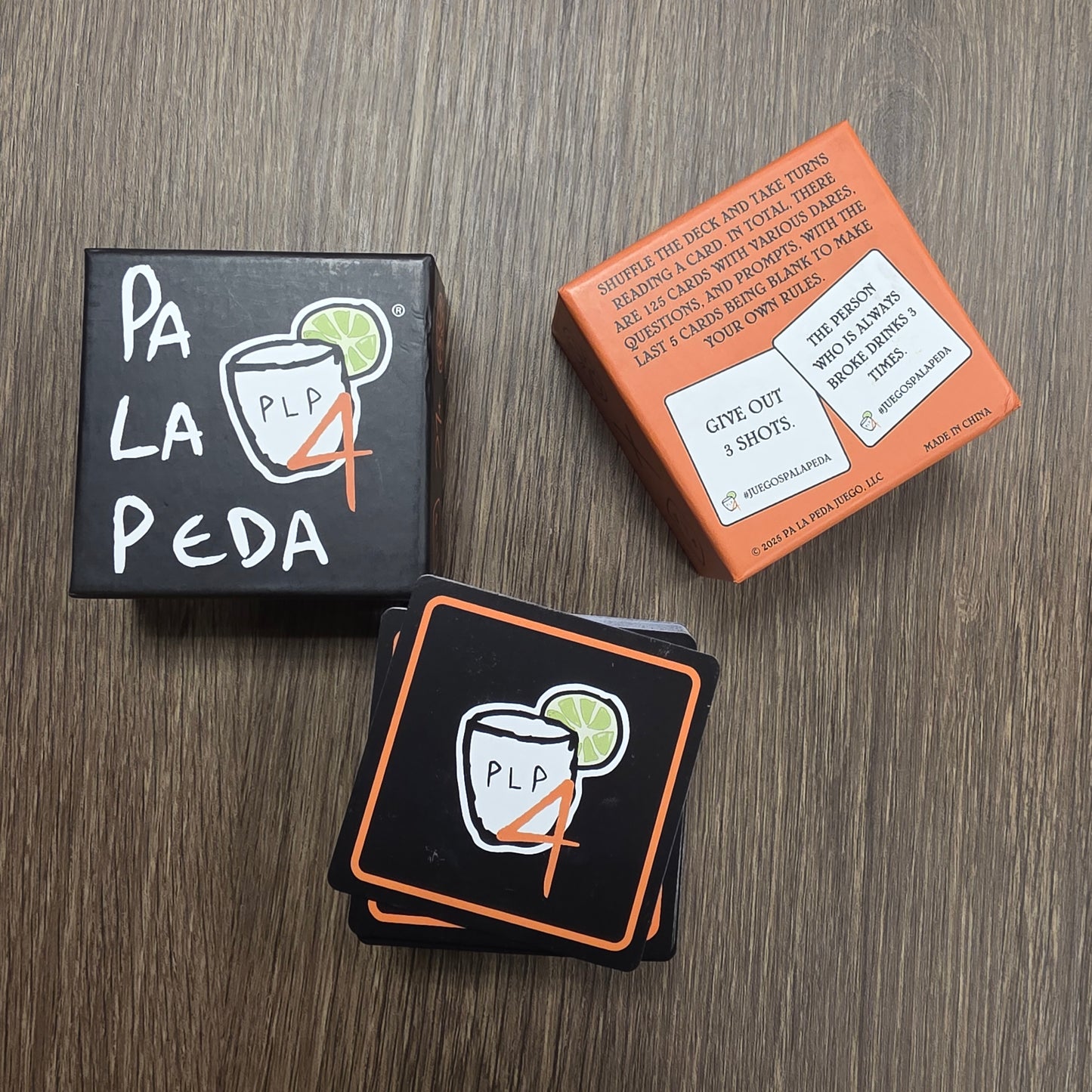 Two boxes and a stack of cards with 'Pa La Peda' branding on a wooden surface.